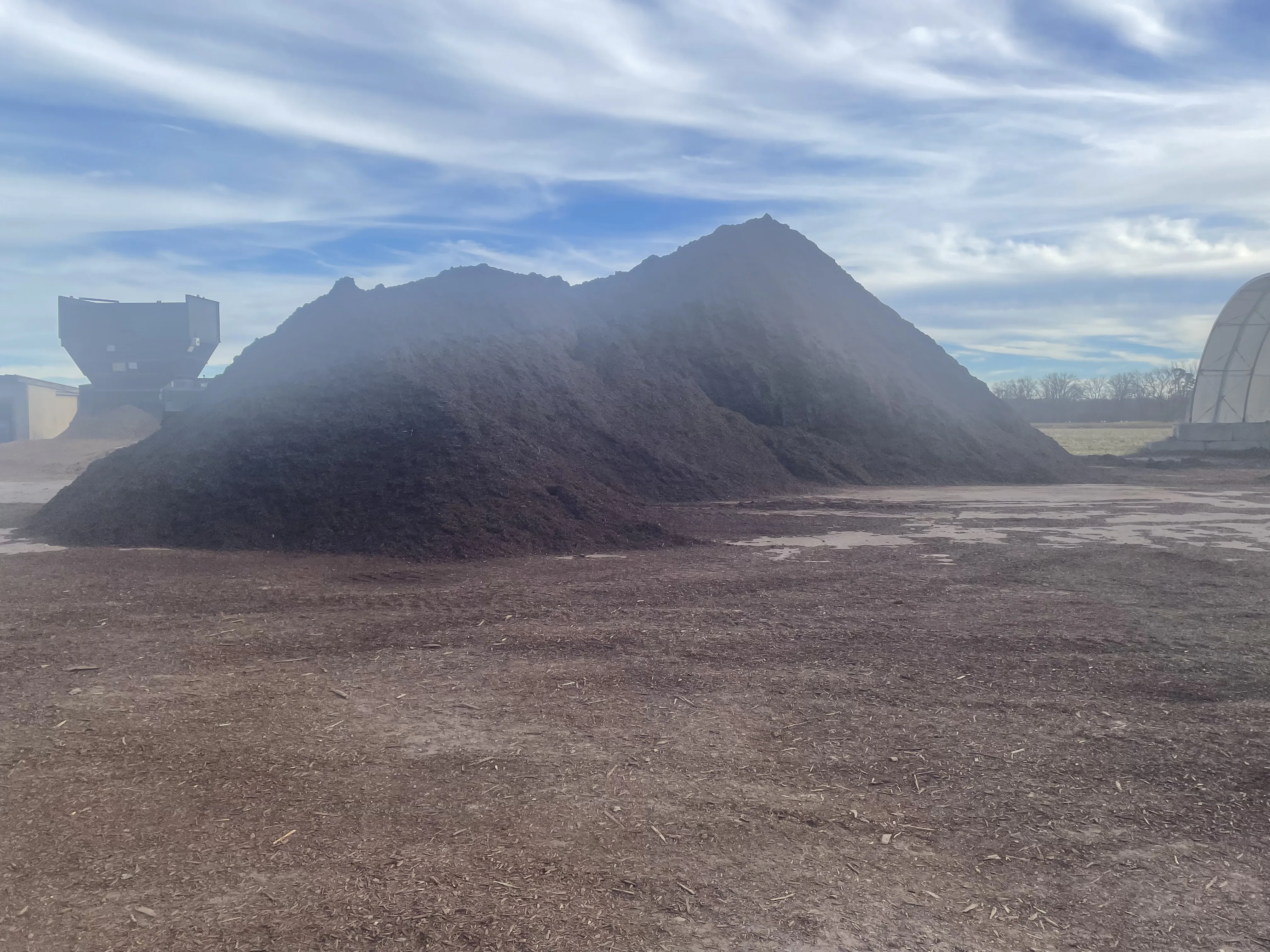 Large pile of dark soil under a cloudy sky