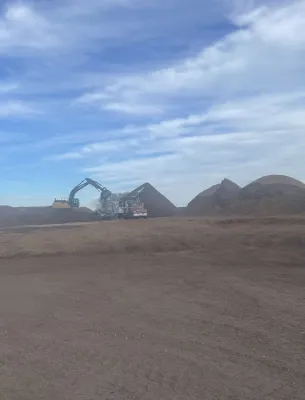 Excavator working with soil piles in an open field